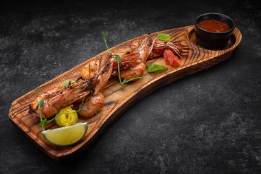 Izgara karides, ahşap bir tahtada, soslu, karanlık bir arka planda.