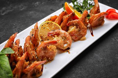 Sarımsak-soya soslu kızarmış karides, susam tohumlu, beyaz tabakta, koyu arkaplanda.