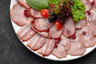 İnce dilimlenmiş sosis, pastırma, haşlanmış domuz eti, et, marul, fesleğen, kiraz, domates ve nar çekirdeği, beyaz bir tabakta.