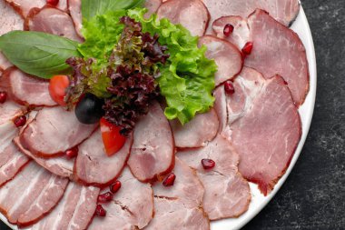 İnce dilimlenmiş sosis, pastırma, haşlanmış domuz eti, et, marul, fesleğen, kiraz, domates ve nar çekirdeği, beyaz bir tabakta.