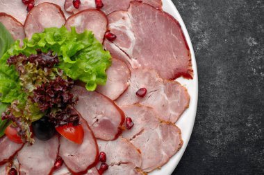 İnce dilimlenmiş sosis, pastırma, haşlanmış domuz eti, et, marul, fesleğen, kiraz, domates ve nar çekirdeği, beyaz bir tabakta.