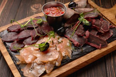 Sosis, sosis, basturma, tütsülenmiş et, sos ve zeytin, ahşap bir tahtada, ahşap bir arka planda.