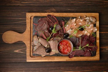 Sosis, sosis, basturma, tütsülenmiş et, sos ve zeytin, ahşap bir tahtada, ahşap bir arka planda.