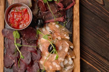 Sosis, sosis, basturma, tütsülenmiş et, sos ve zeytin, ahşap bir tahtada, ahşap bir arka planda.