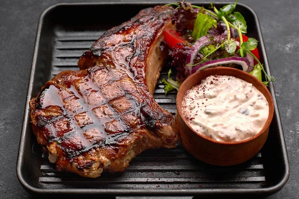 Grilled steak with sauce, vegetables and herbs, on a black frying pan, on a dark background