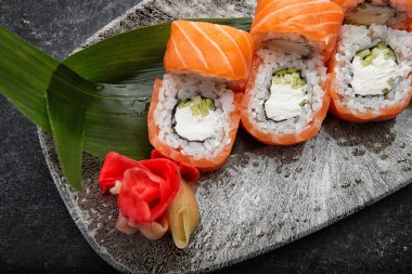 Kaliforniya suşi rulosu, salatalık krem peyniri ve somon gri bir tabakta koyu bir arka planda.