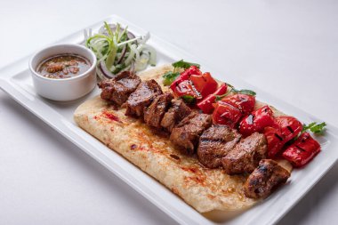 Salamura soğan soslu pide şiş kebap ve beyaz tabakta fırında dolma biber.