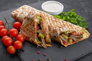 Shawarma ile et, kesme, sos, domates, peynir, otlar ve sarımsak, siyah bir arkaplanda