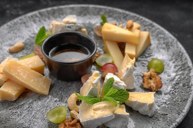 Peynir tabağı, naneli çeşitli peynirler, şekerli meyve, bal ve kurabiyeler, bir tabakta, koyu bir arka planda.