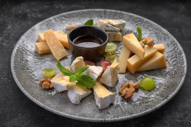 Peynir tabağı, naneli çeşitli peynirler, şekerli meyve, bal ve kurabiyeler, bir tabakta, koyu bir arka planda.