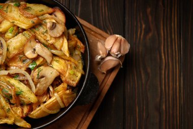 Ev yapımı kızarmış patates, soğanlı, mantarlı ve sarımsaklı, tavada, ahşap bir tahtanın üzerinde.