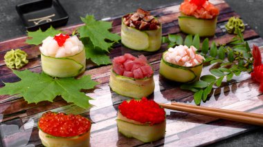 Salatalıklı Gunkan maki, havyarlı, ton balıklı. İstiridye, yılan balığı, karides, yılan balığı ve somon, ahşap bir tahtanın üzerinde, akçaağaç ve akasya yapraklarıyla, sığ bir tarla derinliğinde.