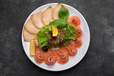 Balık, ince dilimlenmiş, escolar, tereyağlı, somon, fesleğen ve marullu beyaz bir tabakta, koyu bir arka planda.