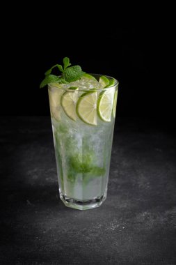 Mojito kokteyli, buzlu, limonlu ve naneli, siyah bir zemin üzerinde, çevresi olmayan, dikey, sığ bir alan.