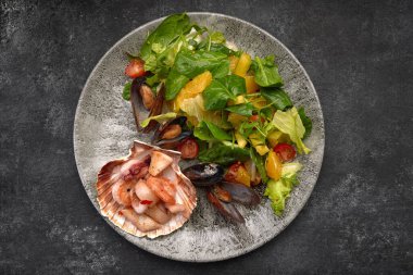 Seafood salad with pineapple and oranges on a plate, on a dark background