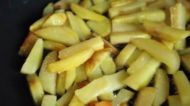 Patates parçaları dökme demir bir tavada yağda kızartılıyor ve yağ kaynıyor..