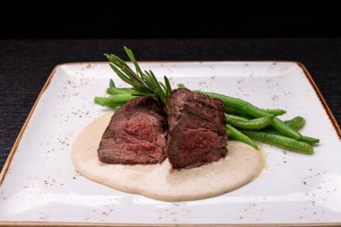 Filet mignon with asparagus on a light plate, on a dark background