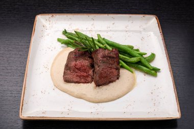 Filet mignon with asparagus on a light plate, on a dark background