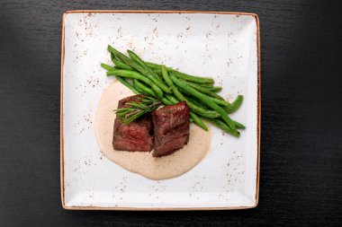 Filet mignon with asparagus on a light plate, on a dark background