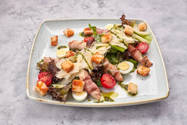 Caesar Salat mit Kräutern Hühnerspeck Eier und Tomaten auf einem quadratischen hellen Teller, auf hellem Hintergrund — Stockfoto