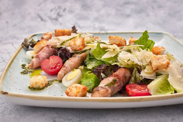 Caesar Salat mit Kräutern Hühnerspeck Eier und Tomaten auf einem quadratischen hellen Teller, auf hellem Hintergrund — Stockfoto