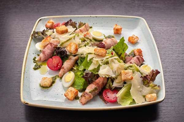 Caesar Salat mit Kräutern Hühnerspeck Eier und Tomaten auf einem quadratischen hellen Teller, auf dunklem Hintergrund — Stockfoto