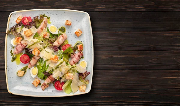 Caesar Salat mit Kräutern Hühnerspeck Eier und Tomaten auf einem quadratischen hellen Teller, auf dunklem Hintergrund — Stockfoto