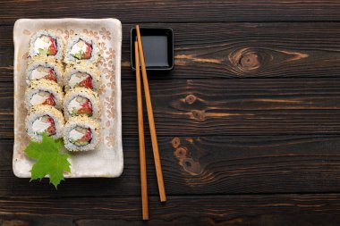 Krem peynirli, pirinçli ve somonlu suşi ruloları koyu ahşap arka planda zencefille süslenmiş bir tahta üzerinde. Japon mutfağı. Yemek fotoğrafı.