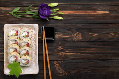 Krem peynirli, pirinçli ve somonlu suşi ruloları koyu ahşap arka planda zencefille süslenmiş bir tahta üzerinde. Japon mutfağı. Yemek fotoğrafı.