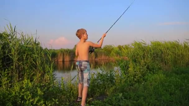 Niño en la orilla del río al amanecer lanza una varilla giratoria — Vídeos de Stock