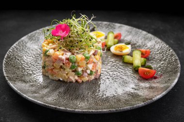 Olivier salatası gri güzel bir tabakta, koyu bir arka planda. Restoran servisi