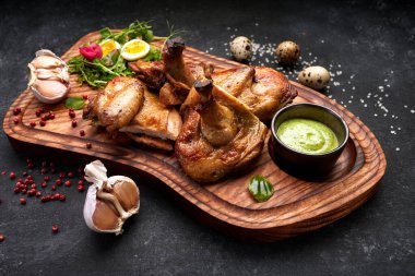 Tahtaya otlar ve sosla ızgara piliç. Siyah bir arkaplanda