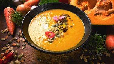 Delicious pumpkin cream soup in a bowl surrounded by fresh ingredients for healthy food photography.