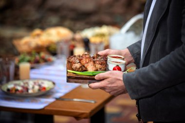 Ahşap tahtada taze et parçaları tutan bir adam, arkadaşlarıyla açık hava toplama konsepti ve sıcak kırsal atmosfer..