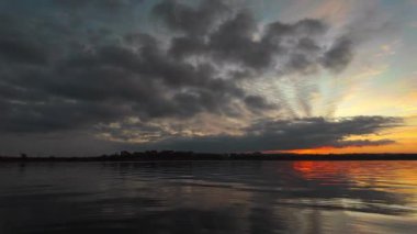 Canlı renkleri ve huzurlu atmosferik manzarası olan sakin bir göl üzerinde büyüleyici sıcak bir gün batımı. Sinema ve doğa temalı görseller için mükemmel..