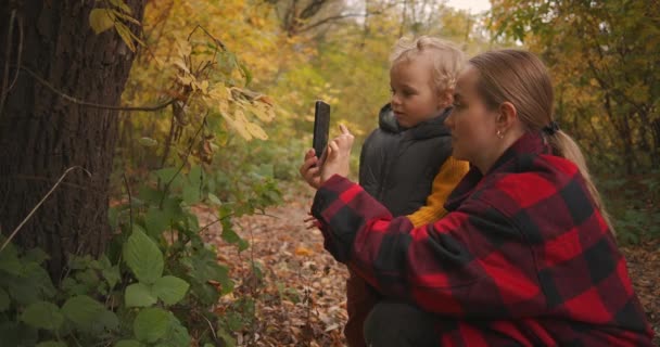 Mãe está ensinando seu filho a tirar foto por smartphone uma natureza, viagem em família na floresta de outono ou parque — Vídeo de Stock