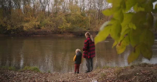 Спокойные выходные на природе, женщина и ее маленький сын любуются лесным озером в осенний день, гуляя и отдыхая в лесу или парке — стоковое видео