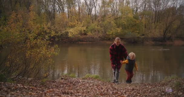 Casual stijl kleding voor moeder en kind voor wandelen in de natuur en actieve rust, vrouw en jongen lopen op de kust van het meer — Stockvideo