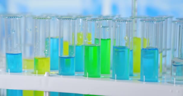 Científico inyectando sustancias químicas en tubos de ensayo. Tubo de ensayo de líquido coloreado en la mesa de laboratorio en el fondo de los frascos de vidrio. vertido de la pipeta de vidrio en el tubo de ensayo iluminado con luz azul — Vídeos de Stock