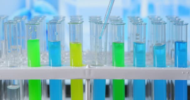 Laboratoriumassistent voegt groene vloeistof toe in de reageerbuis, controleert chemische reactie. Technicus druppelt de oplossing zorgvuldig uit de pipet in glazen buizen voor DNA-analyse. Farmaceutisch laboratorium — Stockvideo