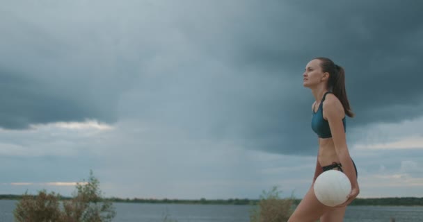 Junge Sportlerin im Bikini spielt Beachvolleyball, mittlerer Schuss gegen malerischen bewölkten Himmel — Stockvideo