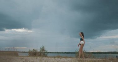 Plaj voleybolu doğada, genç kadın sahada bulutlu gökyüzü, atlet ve sporcu kadına karşı top servis ediyor.