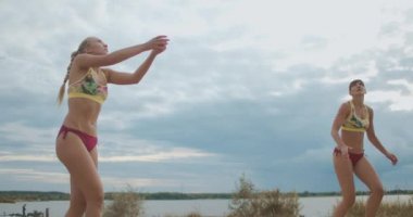 Genç sporcu kadınlar plaj voleybol sahasında antrenman yapıyorlar, atlayıp top oynuyorlar, yarışmaya hazırlanıyorlar.