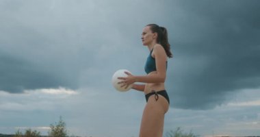 Genç bayan voleybol oyuncusu plaj voleybolu maçında top servis ediyor.
