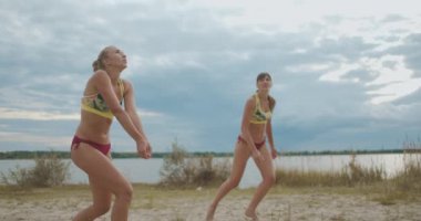 Bayanlar plaj voleybol takımı şampiyonada oynuyor, sporcu kadınlar spor bikini giyiyor, atlıyor ve saldırıyor.