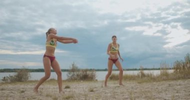 Plaj voleybolcuları dışarıda antrenman yapıyor, iki sporcu kadın geçiyor ve saldırıyor, ağır çekimde.
