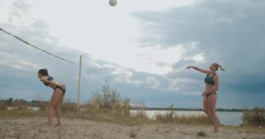 Aktif genç kadınlar yazın bulutlu havalarda plaj voleybolu oynuyorlar, zıplıyorlar ve kumlu sahada koşuyorlar, sağlıklı yaşam tarzları var.