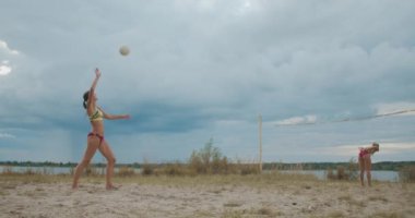 Yaz bulutlu bir günde, plaj voleybol maçında iki bayan takım arasında servis, pas ve saldırı, yavaş çekim