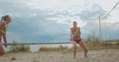 Sportif kadınlar yazın kumsalda voleybol oynuyorlar. İki oyuncu takımı, atletik kadınlar atlıyor.