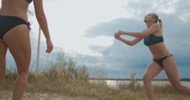 Genç sarışın voleybol oyuncusu kadın plaj voleybolu maçında sayı yapıyor, yavaş çekim, atlama vuruşu.